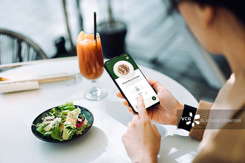 这是一名年轻亚洲女性在餐厅用智能手机上的移动应用订餐。科技让生活变得如此轻松图片素材