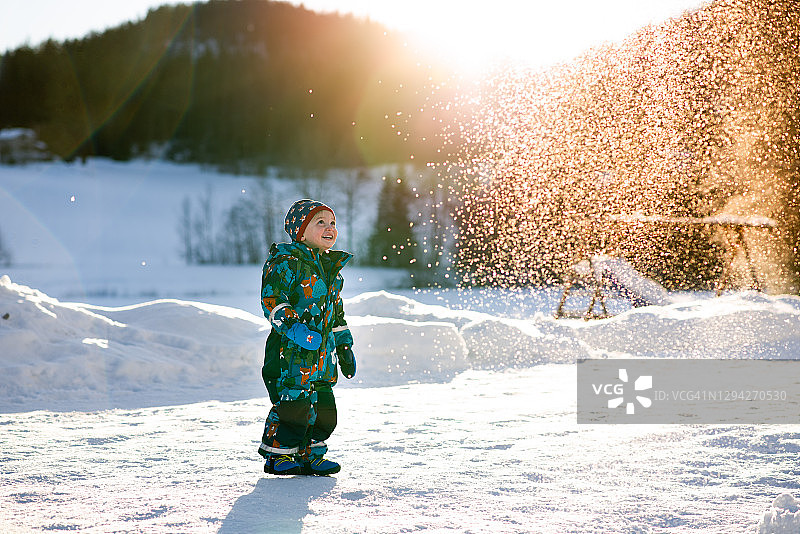 在阳光明媚的冬日仙境里，一个小男孩在农场里看着雪花飘落图片素材