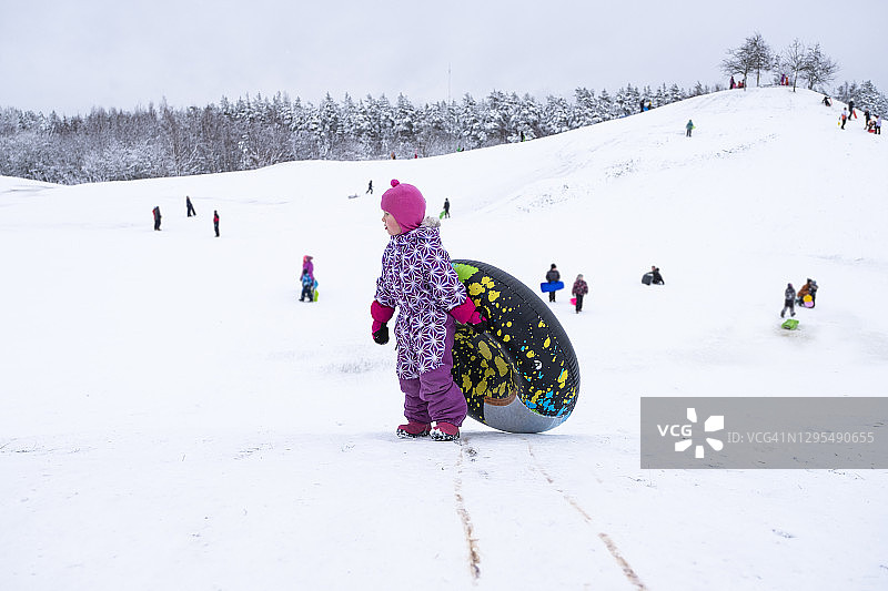 一个小孩，一个5岁的白人女孩，在雪山上玩得很开心，爬上一个充气圈来滑。图片素材