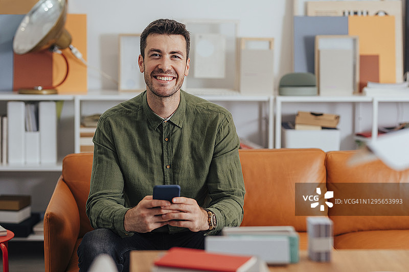 微笑的现代商人坐在办公室里，用他的智能手机进行在线交流图片素材