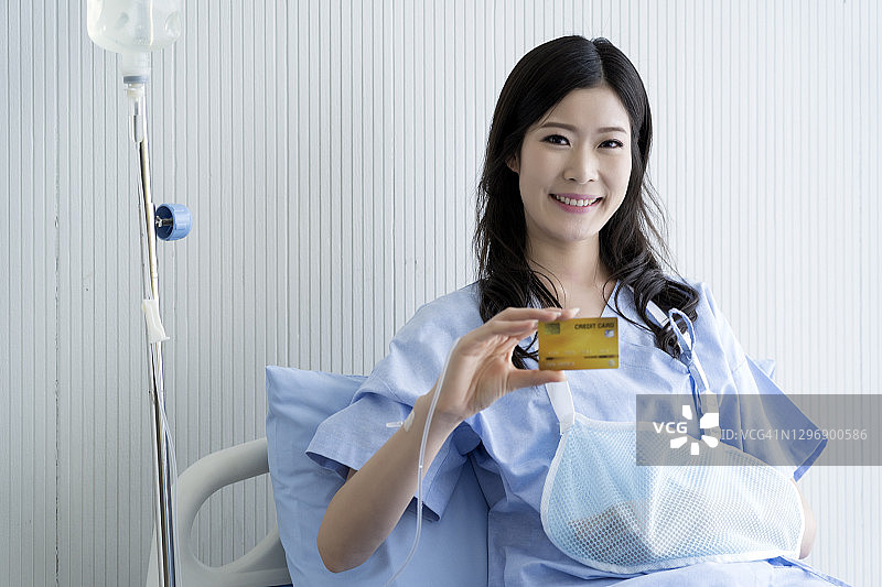 健康保险和支付医疗费用。的概念。幸福的亚洲女人躺在医院的病床上。微笑并出示信用卡。图片素材