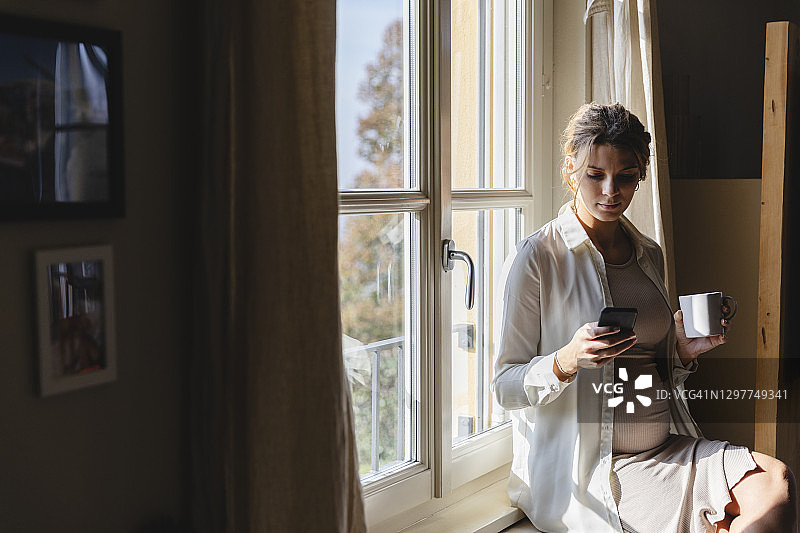 孕妇拿着咖啡杯靠窗发短信图片素材