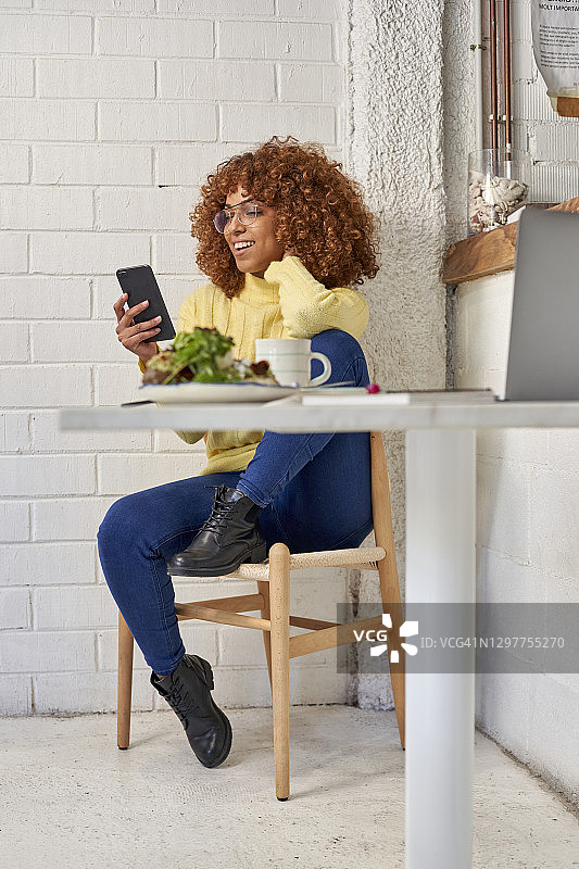 坐在咖啡馆椅子上玩智能手机的快乐女商人图片素材