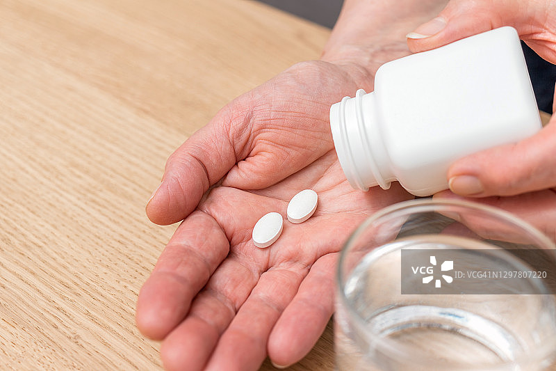 白色止痛片或抗生素用于治疗老年妇女的手掌心，玻璃与水，药品和维生素补充剂的概念，近景图片素材