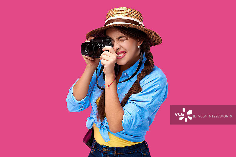 旅游的概念。快乐微笑的女人游客在夏季休闲服装拿着相机拍照，孤立在粉红色的背景与拷贝空间图片素材