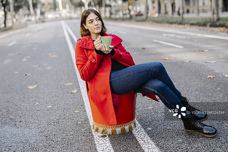 时尚的女人坐在大街上，拿着咖啡杯做白日梦图片素材