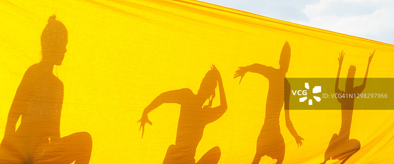 舞者们在阳光明媚的屋顶上一起表演剪影。黄色纺织的现代舞蹈图片素材