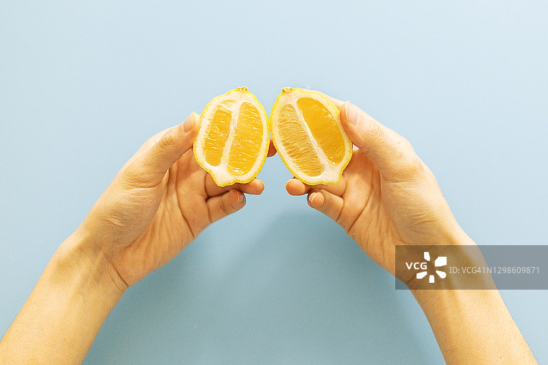 双手握着蓝色背景下的新鲜橙子图片素材