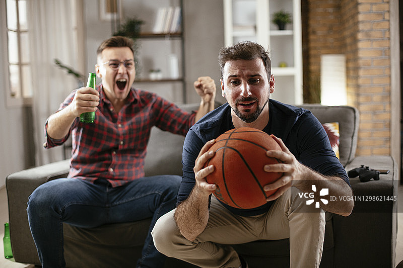男人喝啤酒，看电视上的体育比赛。图片素材