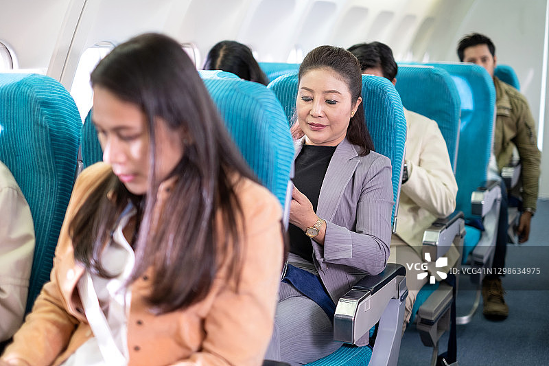 为了安全飞行，女商人坐在飞机上时系好安全带。乘飞机旅行既舒适又安全。安全系统严密。国际航空公司。长途旅行度假图片素材