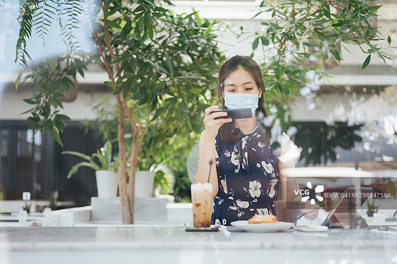 新的。正常的城市生活年轻的亚洲女性商人在户外咖啡馆餐厅用笔记本电脑工作用手机拍摄她的食物在周末。图片素材