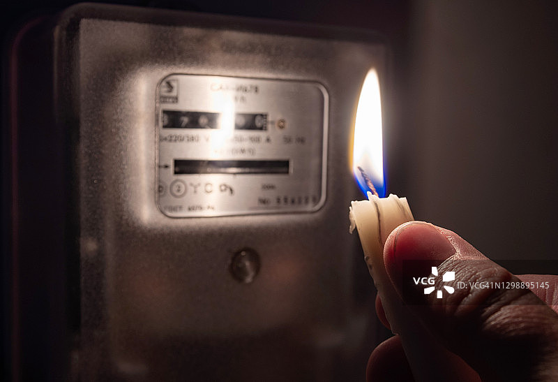 一个男人的手拿着蜡烛在完全黑暗中看着家里的电表。停电，停电概念。图片素材