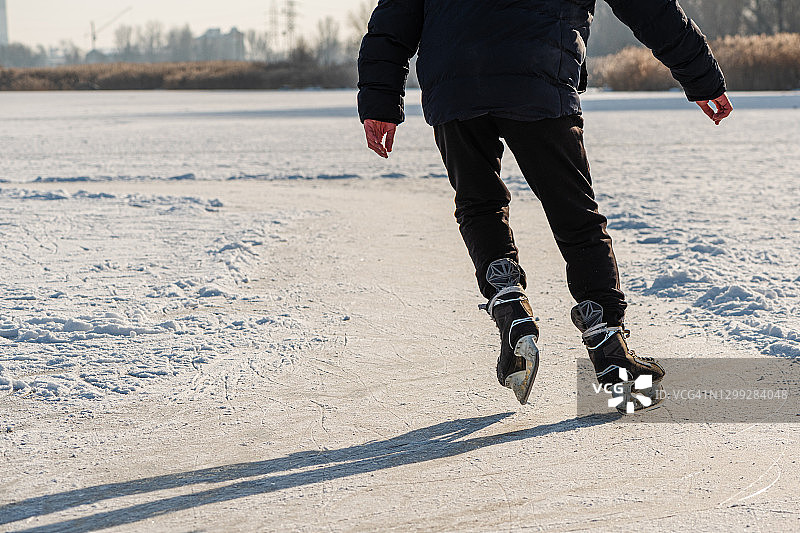 在溜冰场溜冰的人的腿。人们在结冰的湖面上滑冰。后视图。冬季休闲活动。图片素材