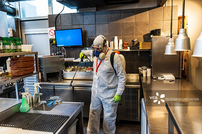 穿着防护服的男子正在为餐厅工作空间消毒图片素材