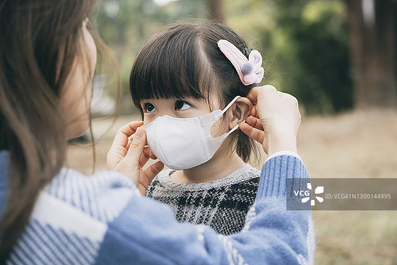 母亲在公园为小女儿戴上外科口罩，防止感冒、流感和病毒的传播图片素材
