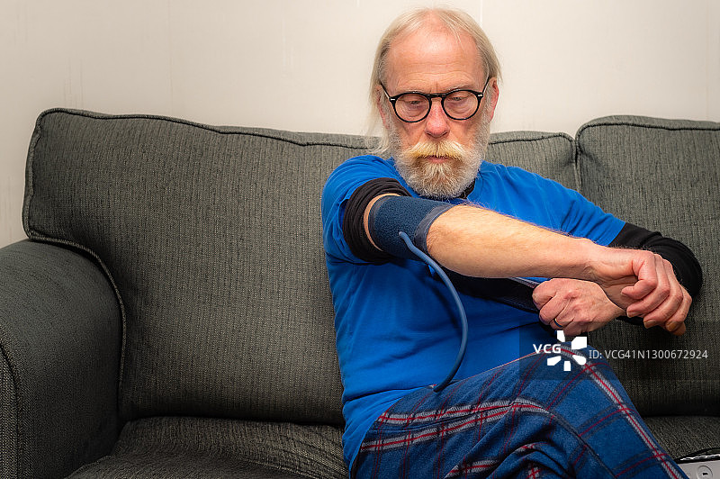 一位老人坐在家里的沙发上，戴上袖口准备测量他的血压图片素材