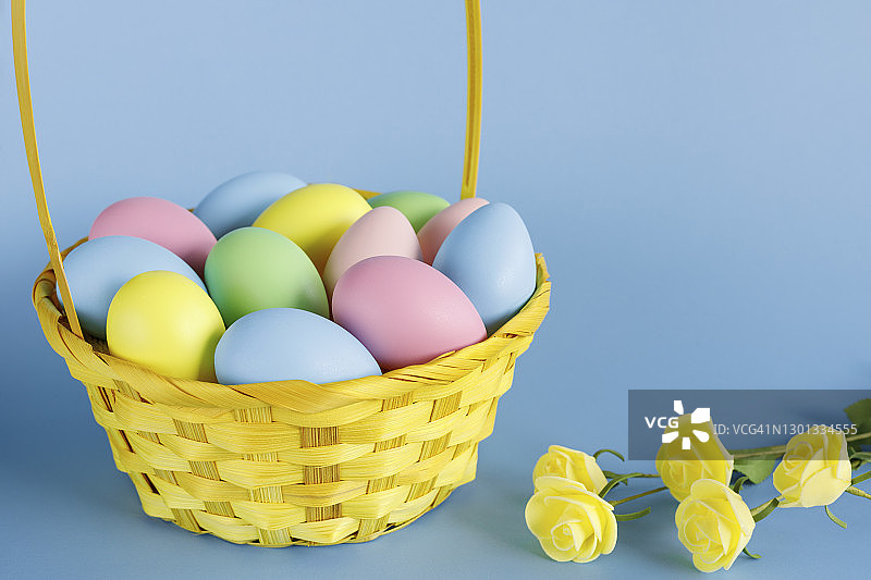 篮子里放着复活节彩蛋，旁边放着小花，并在蓝色背景上复制空间。图片素材