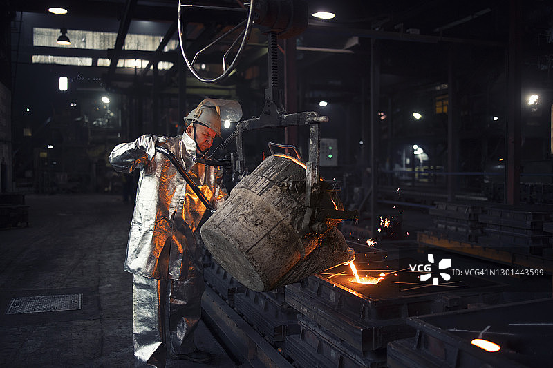 铸铁件在冶炼厂。铸造工人将钢液倒入模具中。图片素材