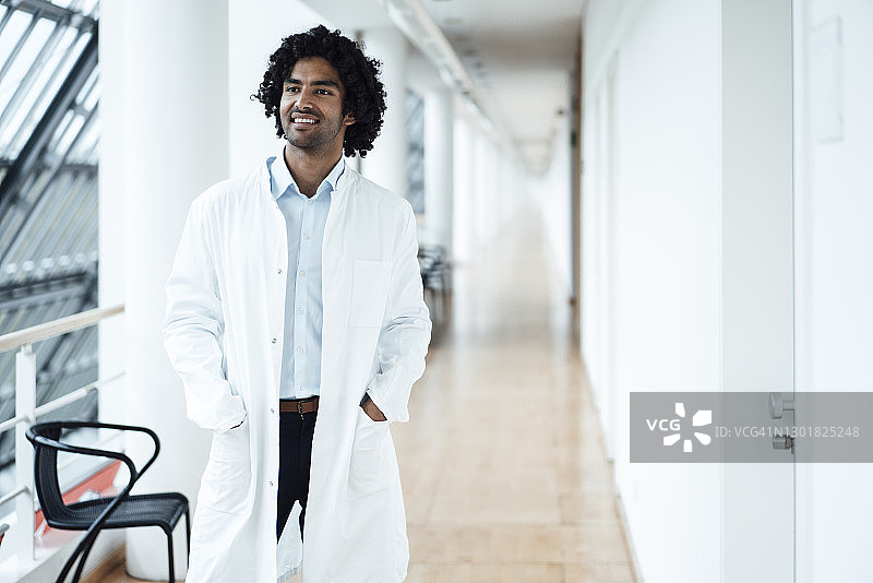 微笑的年轻男医生站在口袋里，看着医院走廊图片素材