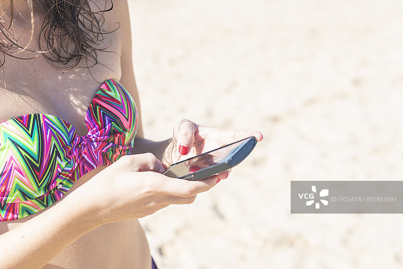 一个在沙滩上玩手机的女人图片素材