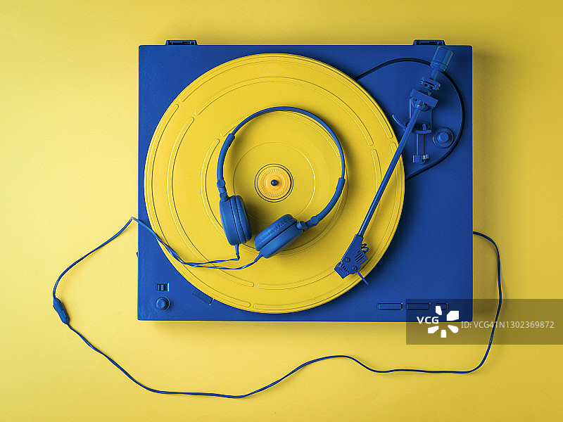 老式的黑胶唱片机和黄色背景上的蓝色耳机。图片素材