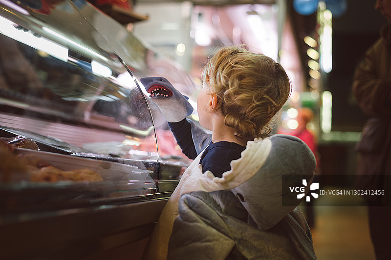 男孩装扮成鲨鱼在市场的肉区玩着一个鲨鱼木偶图片素材