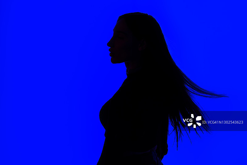 一个年轻女子的剪影长发站在蓝色发光的背景图片素材