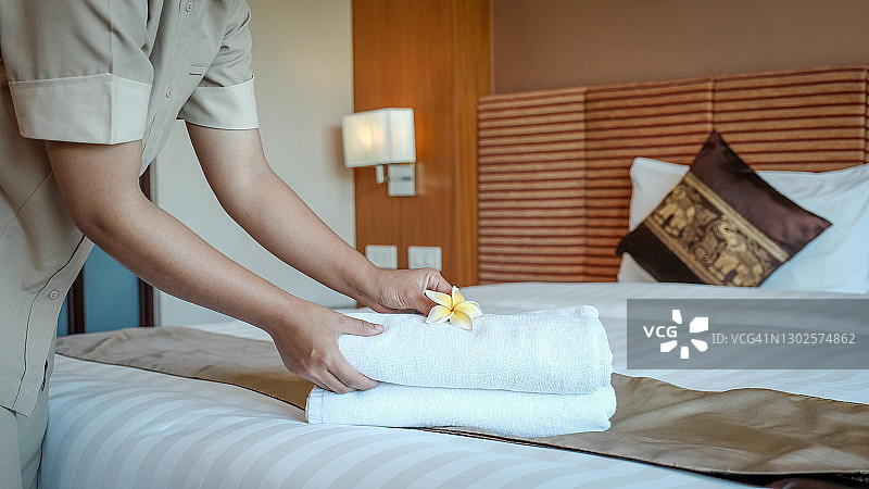 酒店服务员的手把鸡蛋花和毛巾放在豪华酒店房间的床上，为游客旅游做好准备图片素材