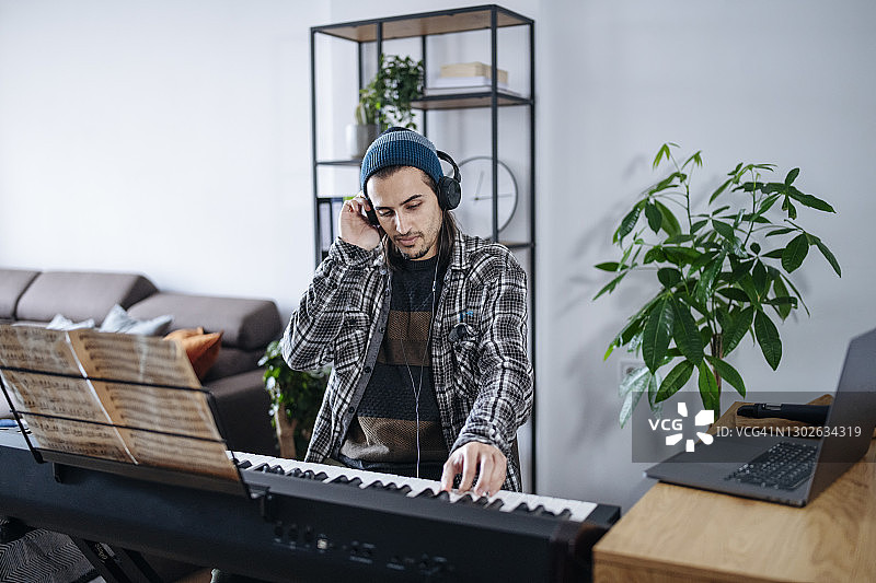 受启发的年轻艺术家戴着耳机在家里弹奏电子钢琴。图片素材