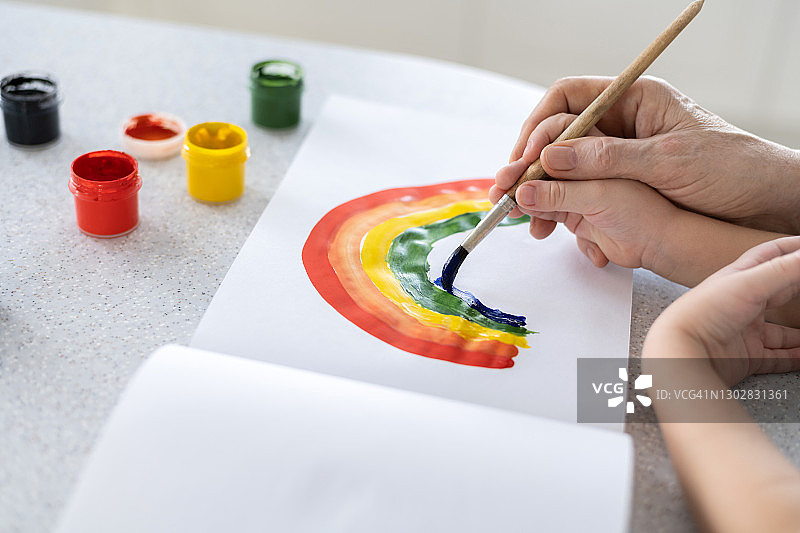 一个孩子的手中在一个成年人的手中学会画彩虹图片素材