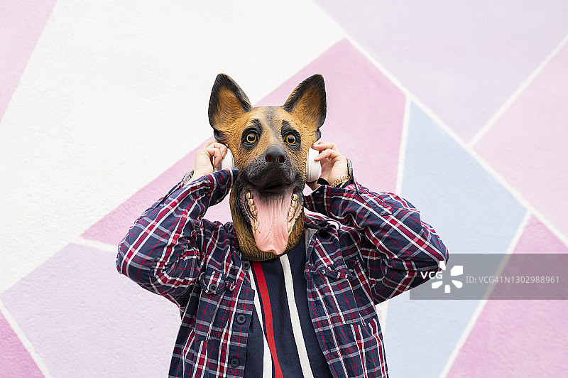 女人戴着狗面具戴着耳机站在多色墙图片素材