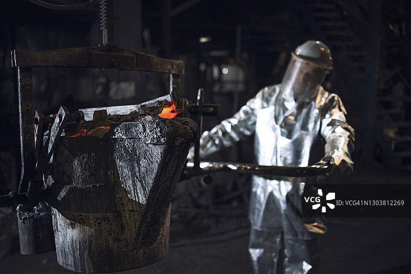 炼钢厂铝化消防防护服的铸造工人推铁液桶。图片素材