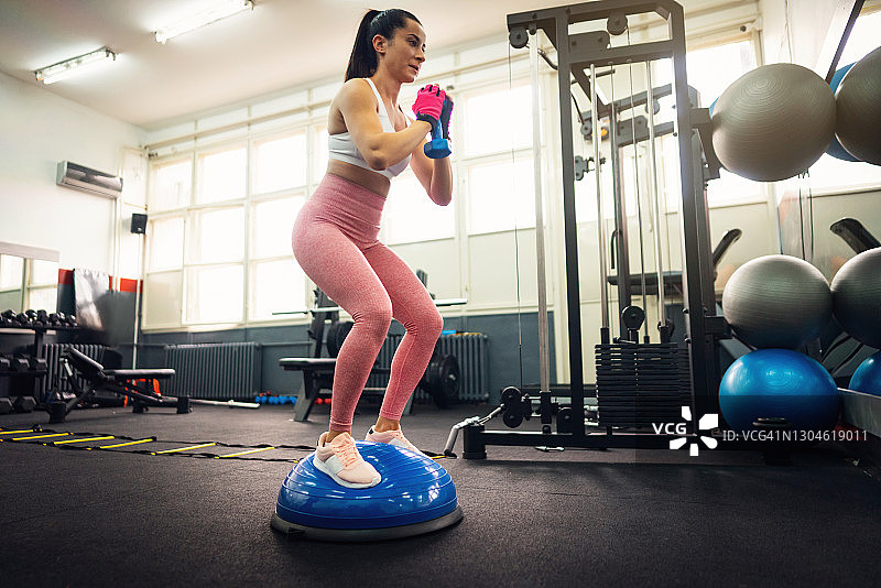 年轻的健康女子运动在蓝色半平衡球在健身房图片素材