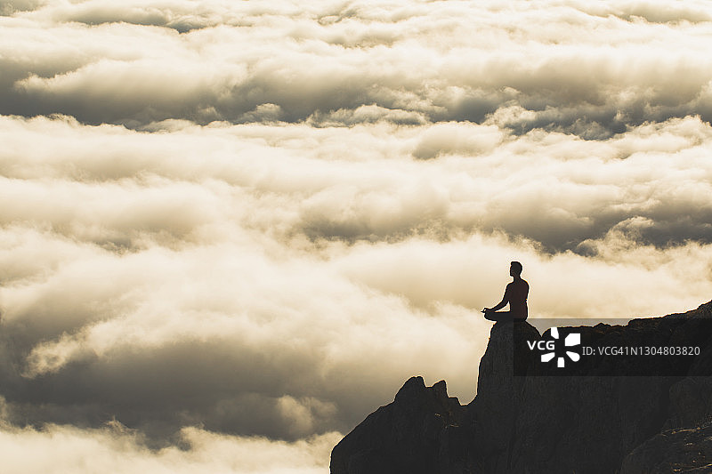 一个人在日落时独自练习瑜伽的剪影在悬崖边缘与令人惊异的低云背景图片素材