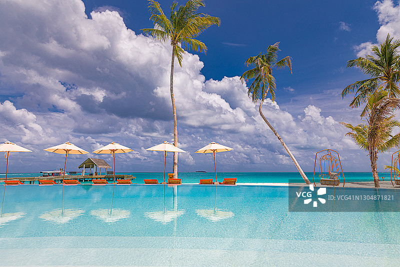 8月的02.。2019年，马尔代夫，达卢环礁，伊鲁维利岛:奢华的海滩度假胜地，配有游泳池和沙滩椅或躺椅，在棕榈树和蓝天的伞下。夏季海岛旅游度假景区图片素材