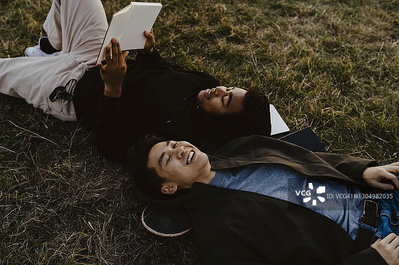 一个年轻人躺在公园的草地上看日记图片素材