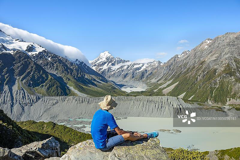 徒步者坐在一块岩石上，观看穆勒湖的胡克谷，胡克湖和库克山，西利塔恩斯小径，胡克谷，库克山国家公园，南阿尔卑斯山，坎特伯雷，南岛，新西兰图片素材