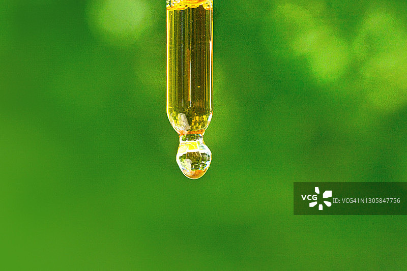 美容产品用透明液体在玻璃移液管上以自然植物为背景。图片素材