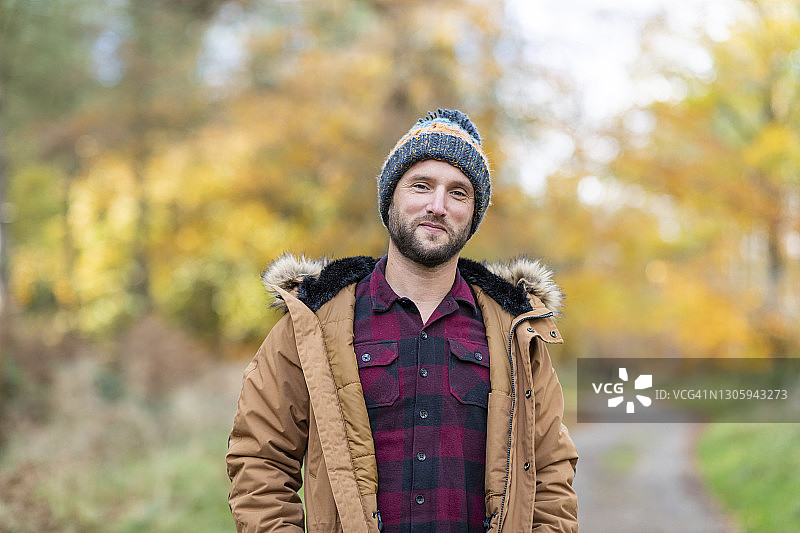 微笑的男人戴着针织帽凝视着站在森林图片素材