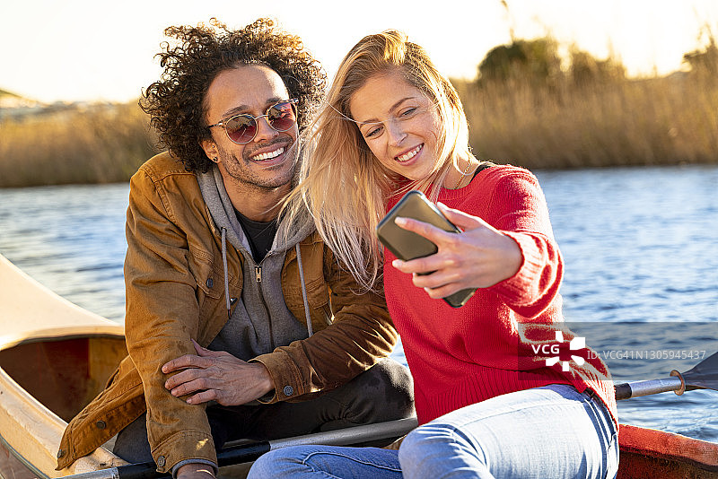 坐在河上的独木舟上，微笑的情侣用手机自拍图片素材