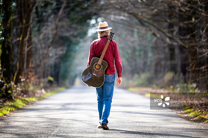 一个背着吉他走在乡间小路上的自由流浪汉图片素材