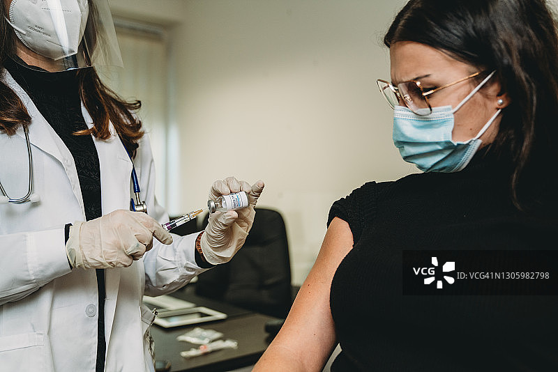 医生正在给一名年轻成年妇女注射Covid-19疫苗图片素材