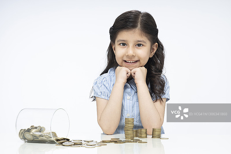 肖像的印度可爱的小女孩与玻璃罐的硬币坐孤立在白色的背景:股票照片图片素材