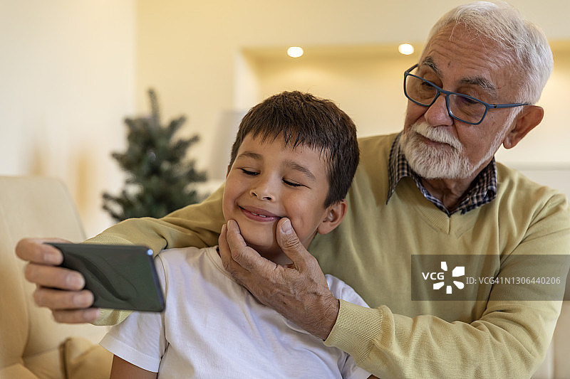 一位快乐的老人和他的孙子在家里微笑着自拍。图片素材