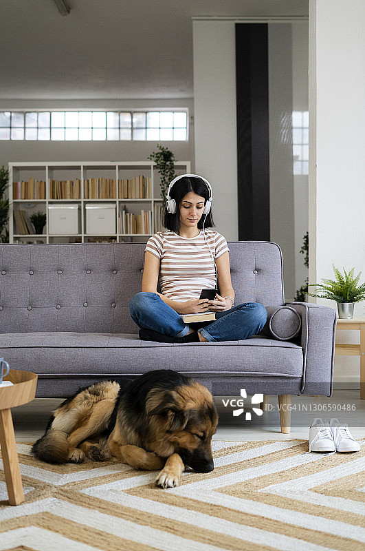 女人坐在沙发上听音乐，而狗睡在客厅的地毯上图片素材