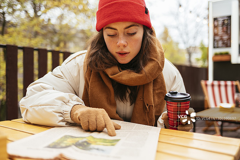 拿着咖啡杯坐在路边咖啡馆看报纸的女人图片素材