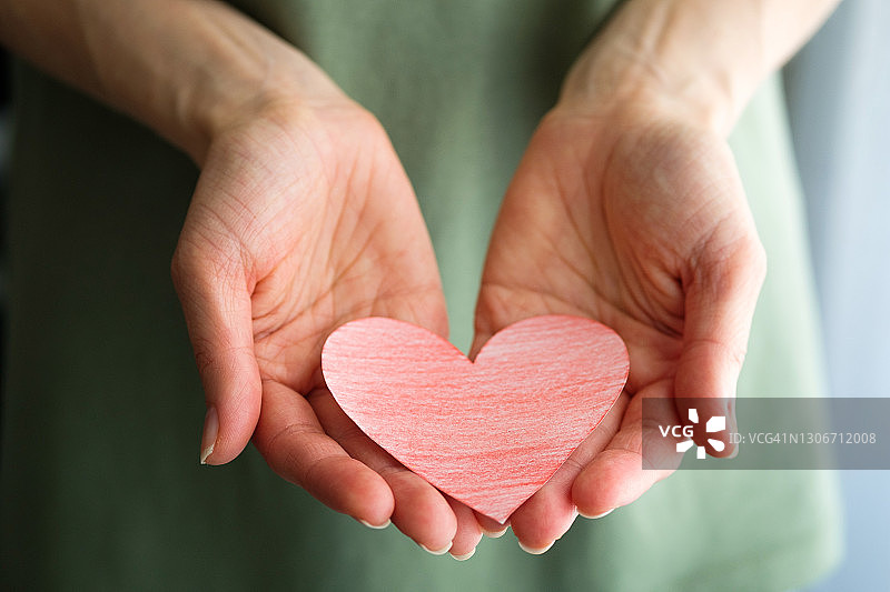 一个女人或女孩拿着一颗红心或一张纸剪成的情人节卡片。以心形为背景的绿色休闲装或t恤。情人节的概念，是爱情和忠诚的象征。图片素材