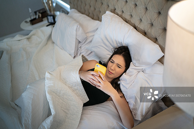 年轻女子躺在床上玩手机图片素材