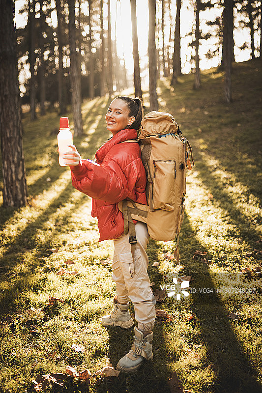 快乐的年轻微笑的女人徒步在大自然的山上，喝着橙汁，享受图片素材