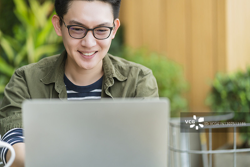 年轻有吸引力的亚洲商人工作与笔记本电脑，而坐在咖啡店咖啡店的户外花园背景图片素材